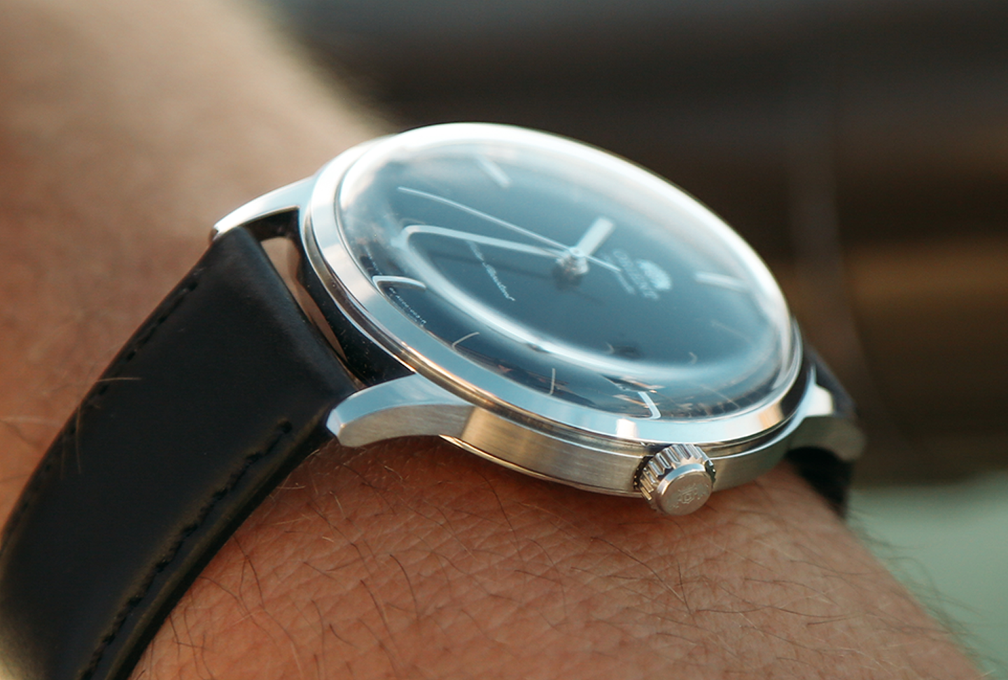 Close-up of a classic analog wristwatch with a black leather strap and silver casing on a wrist. The watch face is dark with minimalist hour markers.