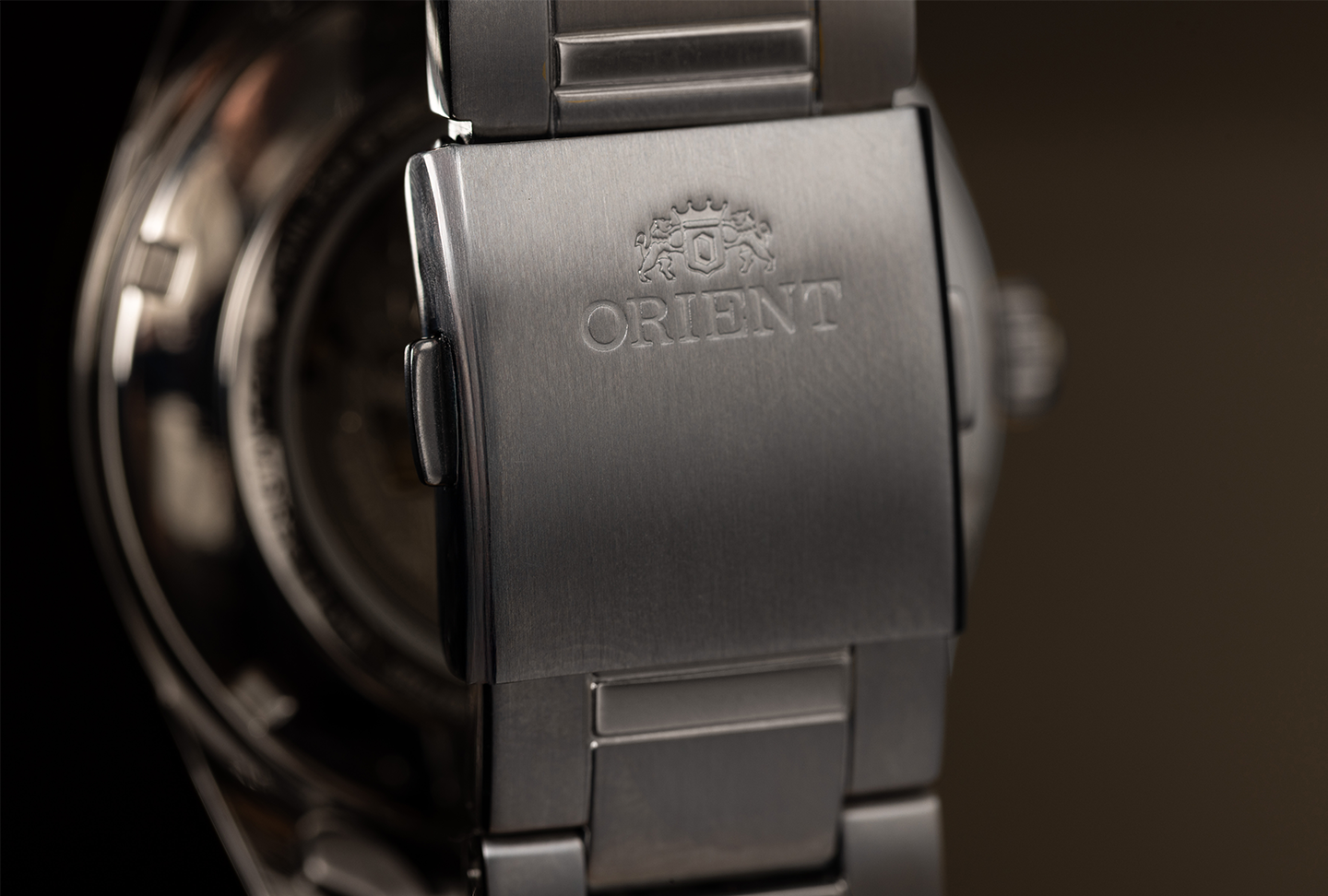 Close-up of a stainless steel watch clasp with "ORIENT" engraved, showing a brushed metal finish and an intricate emblem, conveying elegance.