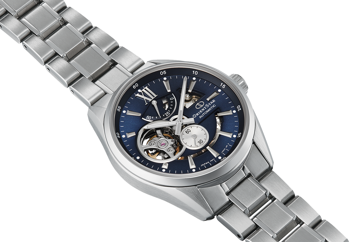 A stainless steel wristwatch with a blue skeleton dial, featuring visible mechanical gears through the case and a matching steel link bracelet, set against a plain white background.

Orient Star RE-AV0003L