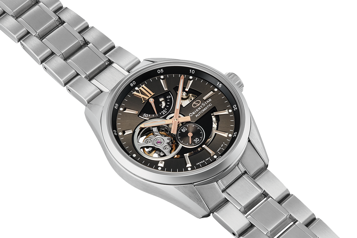 A stainless steel skeleton watch with a dark dial, rose gold-tone hands and markers, and a matching steel link bracelet, shown on a plain white background.

Orient Star RE-AV0004N