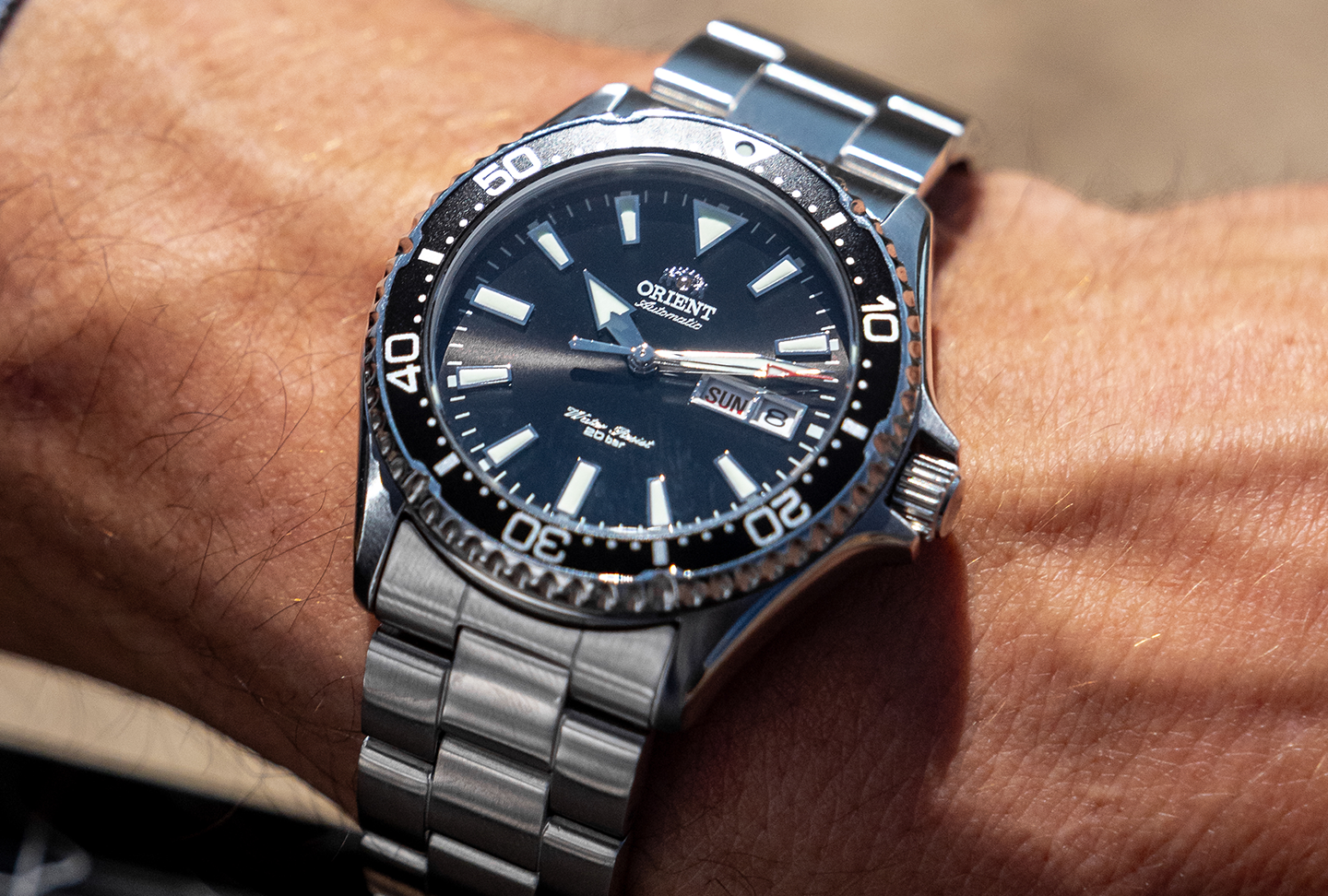 A close-up of a wrist wearing an Orient automatic diver’s watch with a sapphire crystal, stainless steel band, black dial, and day-date display.